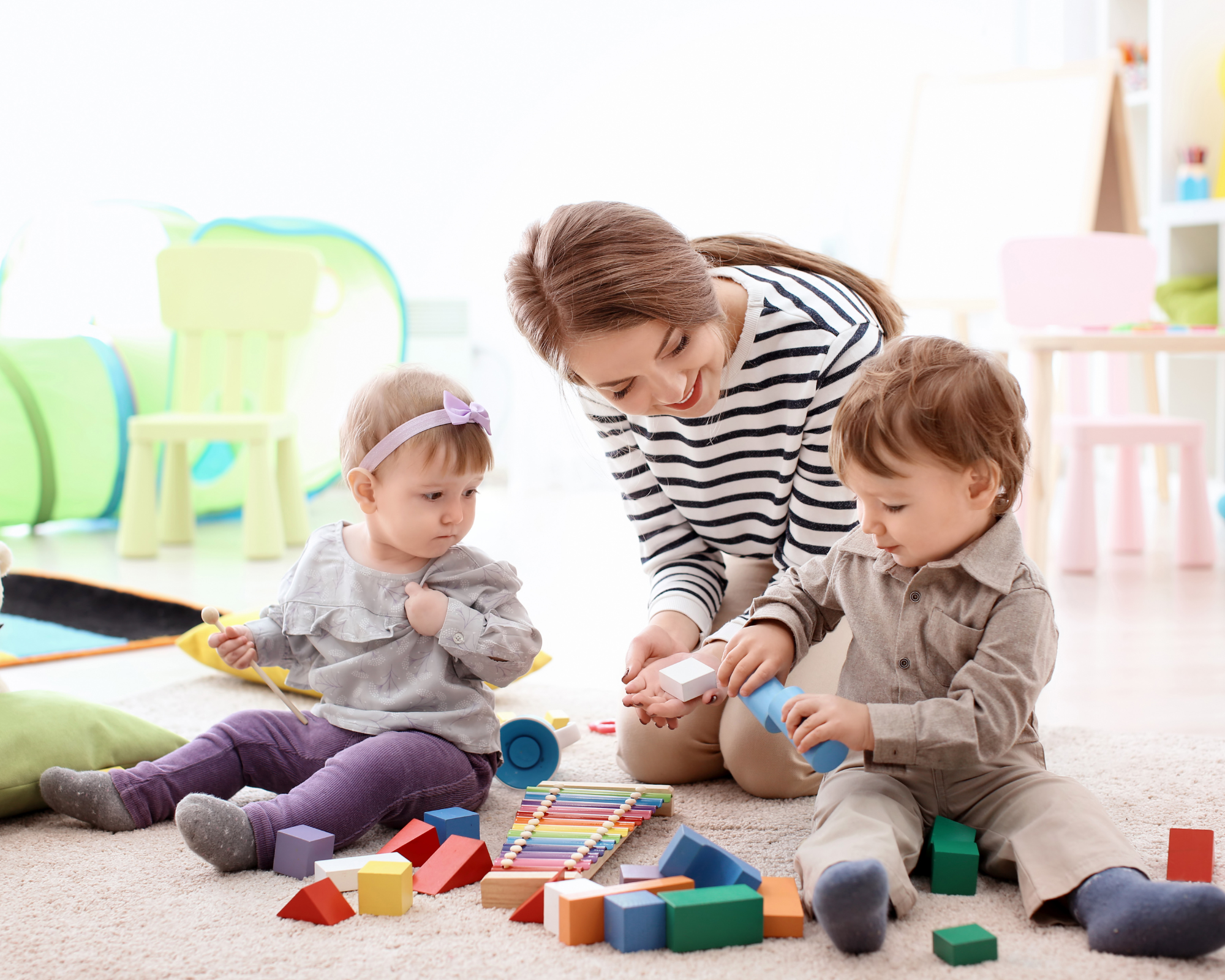 Young woman sitting on floor with two children playing with blocks