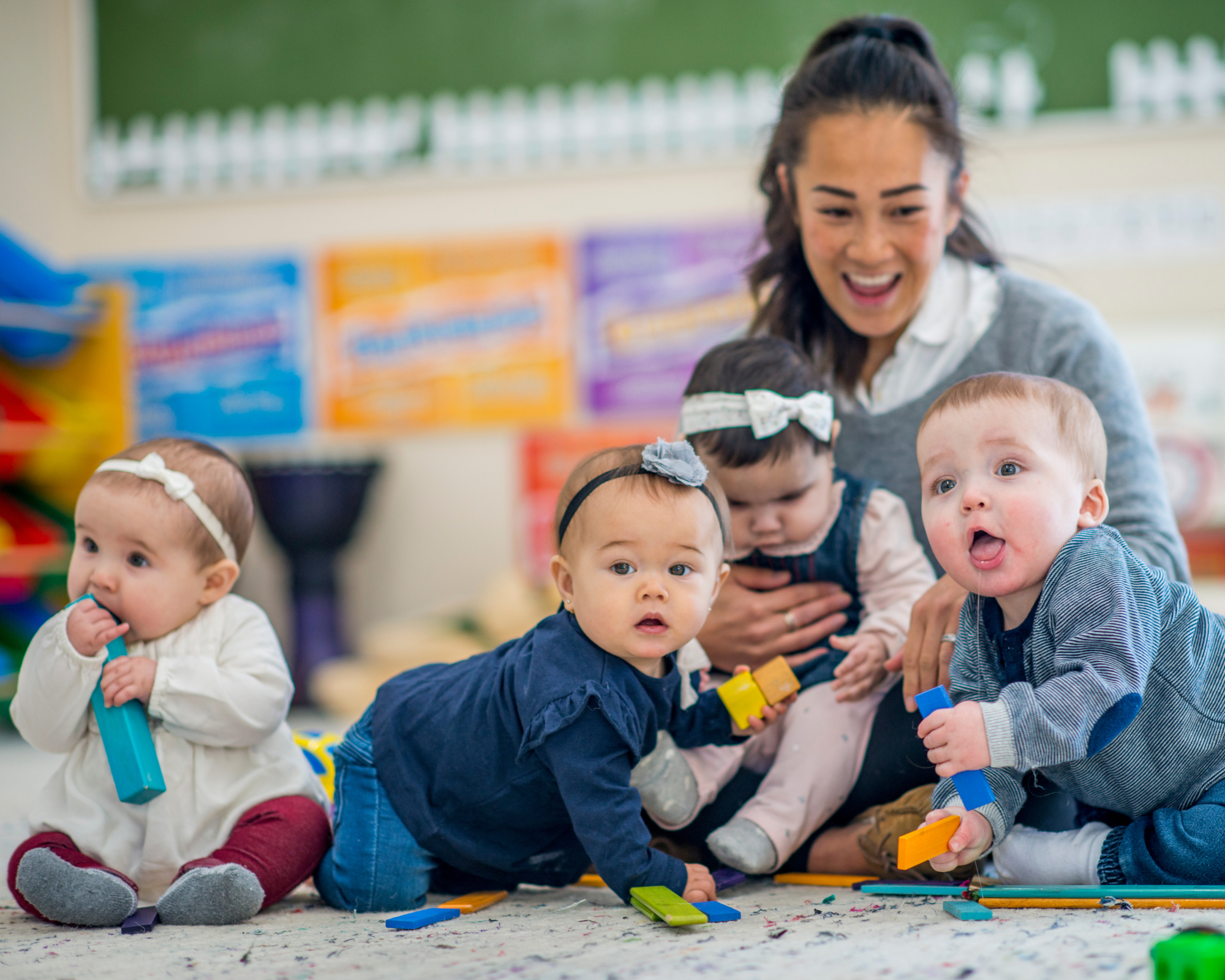 Woman sitting on the floor smiling with four infant children surrounding her as a daycare home provider