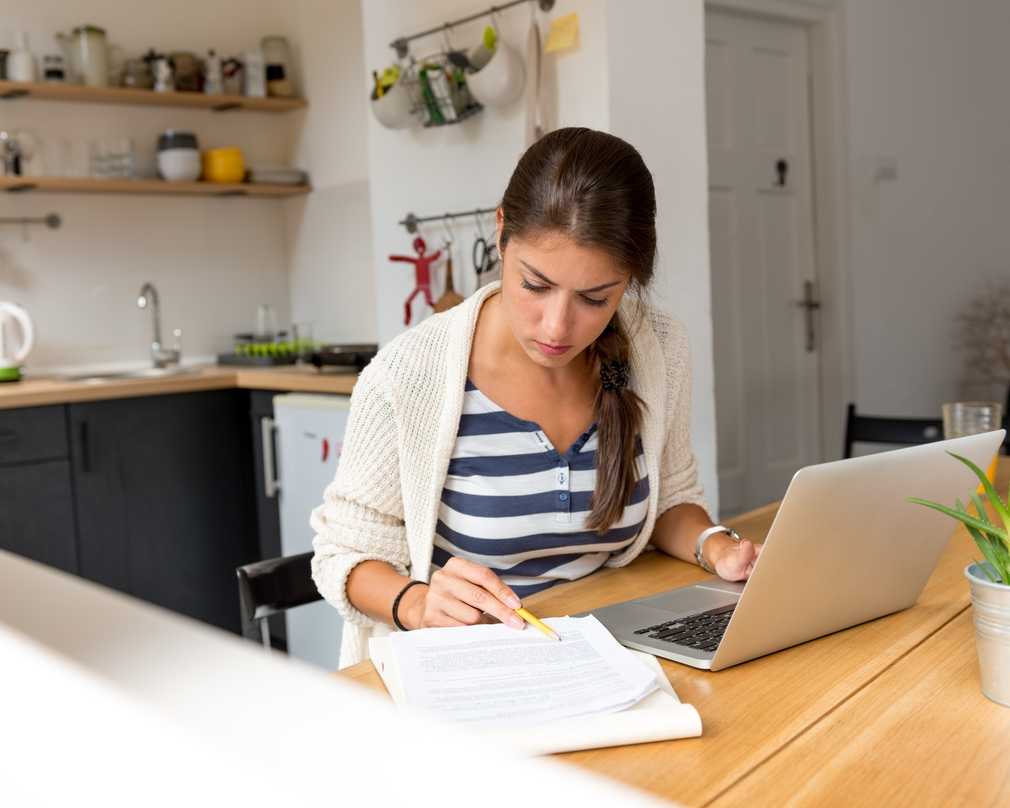 Woman looking at papers on a desk with laptop open learning how to open a successful sleep consultant business