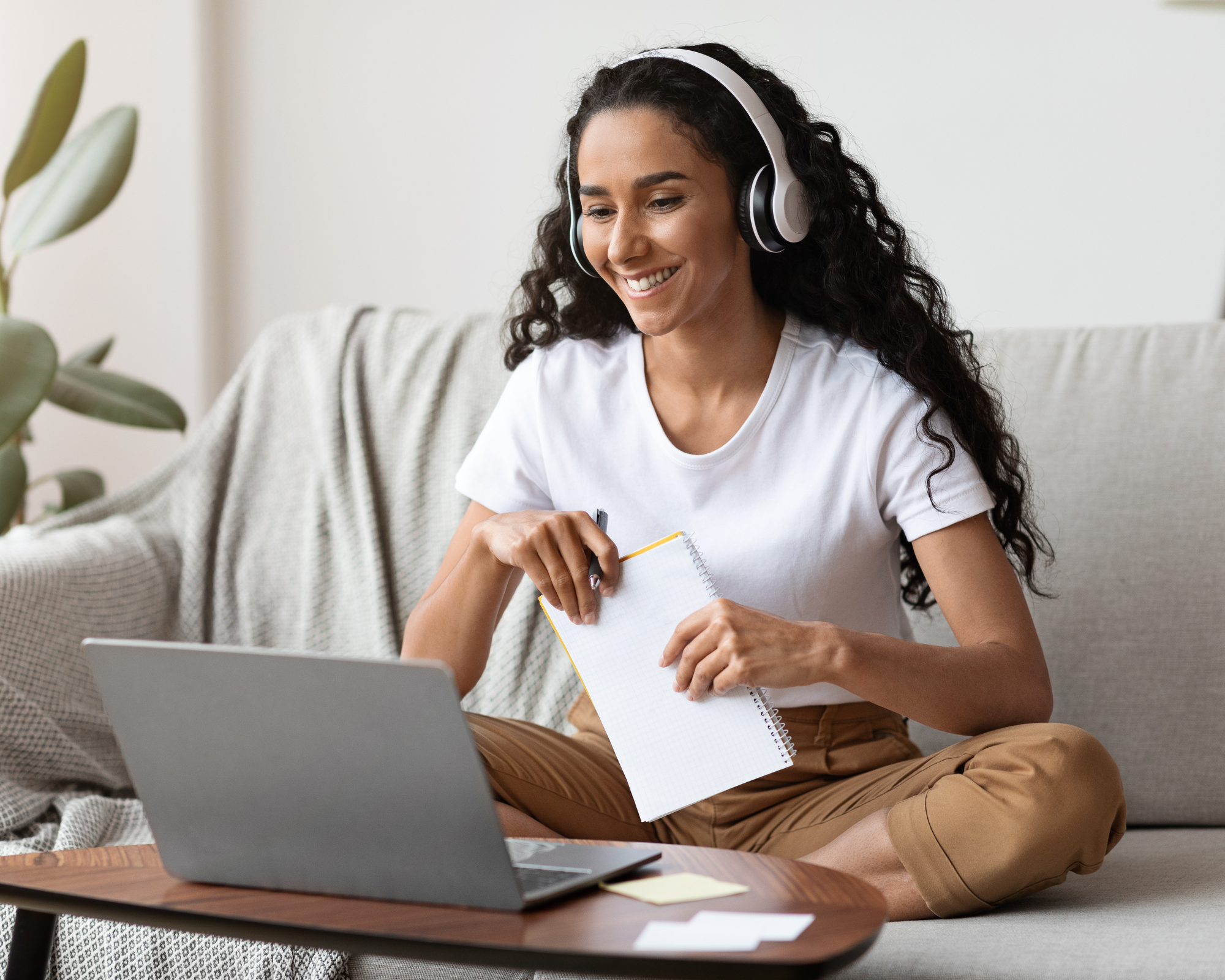 Woman with headphones on looking at a laptop computer screen and smiling. Taking the best sleep consultant course.