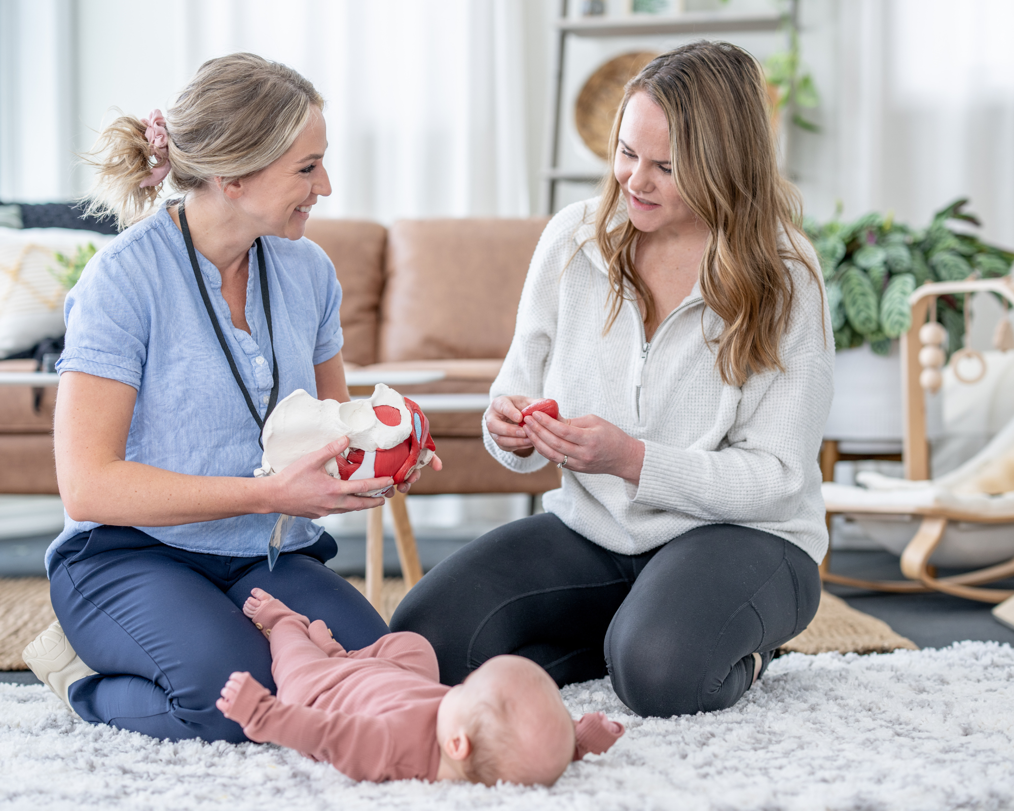 Doula sitting on the ground next to a mother and her baby talking to the mother: How to scale your postpartum doula business