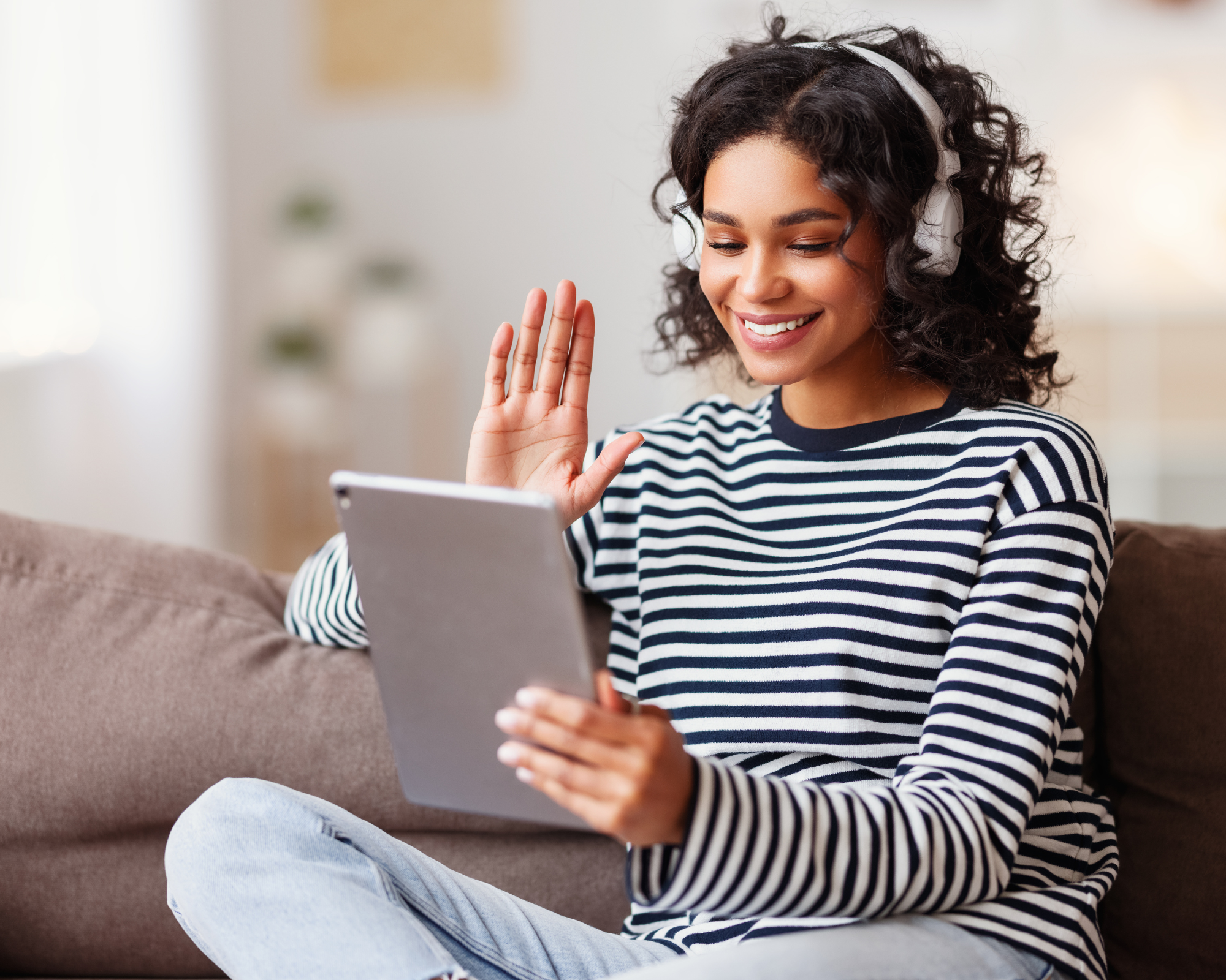 Woman sitting on a couch with headset while holding a tablet and waving to the screen: new sleep consultants