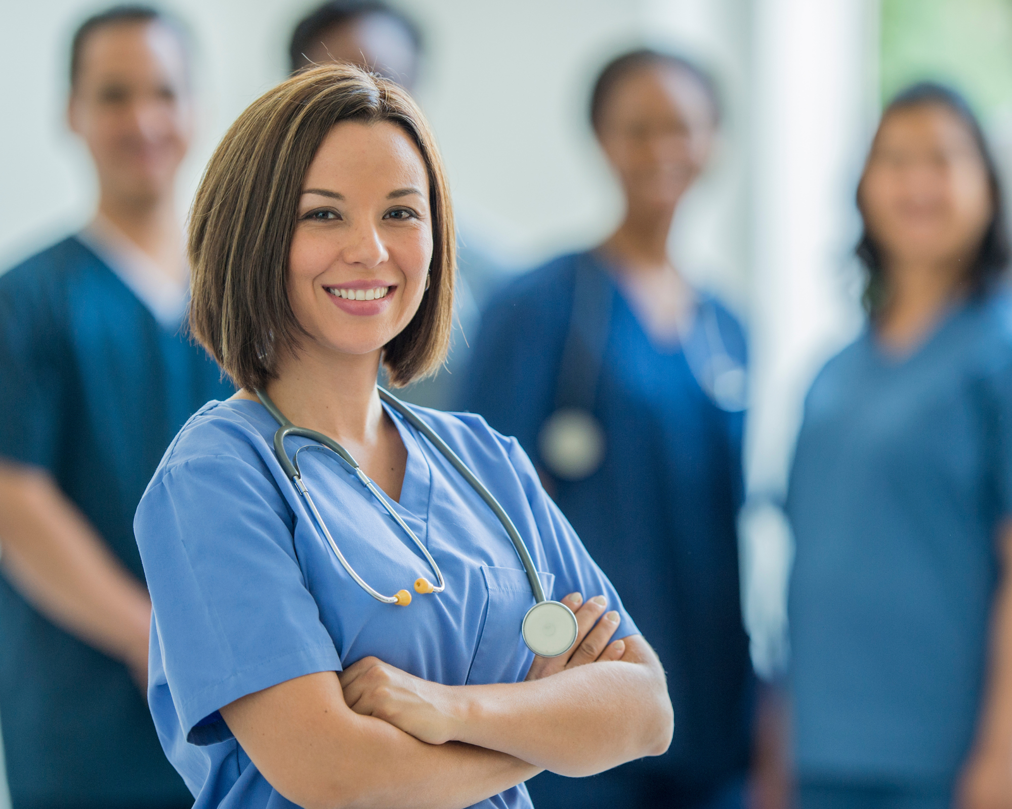 Woman in scrubs standing in front of other medical professionals: side hustle for nurses